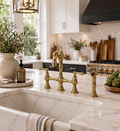 Gold kitchen faucet on a marble countertop with a kitchen in the background
