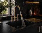 A modern kitchen scene with a matte black double-bowl sink, a tall arched pull-down faucet in brushed gold, and water running from the sprayer. The countertop and backsplash are also black marble or stone, with warm under-cabinet lighting and decorative objects in the background.