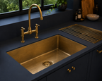 Aged brass bridge kitchen faucet with integrated brass sink in a modern dark kitchen.